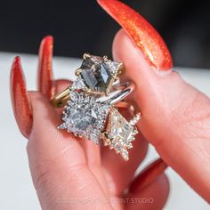 a woman's hand holding three rings with different colored stones on them and an orange manicure