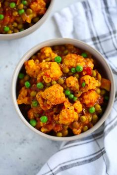 two bowls filled with cauliflower and peas on top of a white table cloth