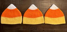 three crocheted orange and white hats on top of a wooden table next to each other