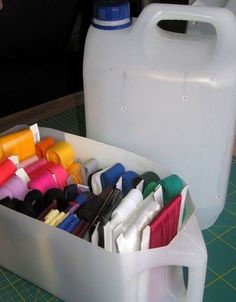 a plastic container filled with lots of crafting supplies next to a white jug on a cutting board