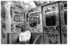 a black and white photo of a man sitting on a subway car covered in graffiti