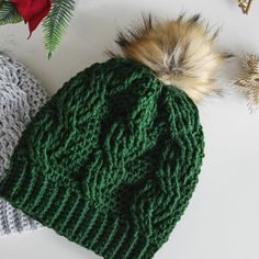 two knitted hats with fur pom poms on top of each other next to christmas decorations