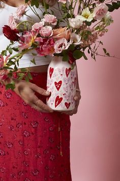 a woman holding a vase with flowers in it and hearts painted on the jar behind her