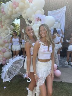 two young women standing next to each other under an arch with balloons and umbrellas