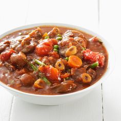 a bowl filled with meat and vegetables on top of a white table next to a spoon