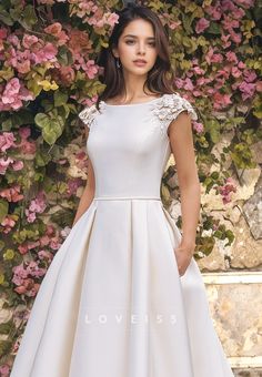 a woman wearing a white dress standing in front of a wall with flowers on it