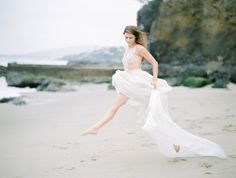 a woman is running on the beach with her dress flowing in front of her,