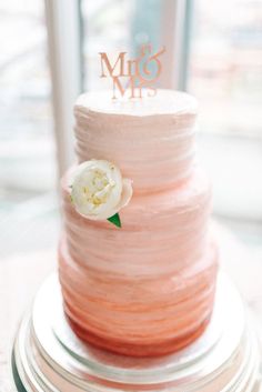 a three tiered pink cake with a white flower on top