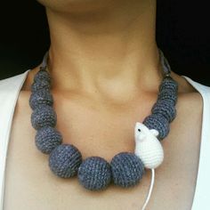 a woman wearing a crocheted necklace with a white and gray bird on it