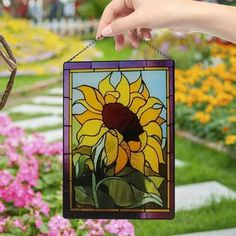 a hand holding a stained glass sunflower ornament in front of some flowers