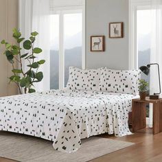 a white bed with green trees on it in a living room next to a window