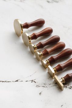 six wooden handles with metal tips on a marble counter top, one is gold and the other is white