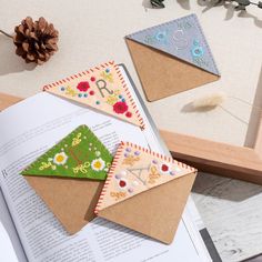 three pieces of paper are sitting on top of an open book, next to a pine cone