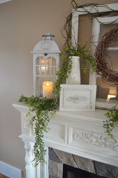 a white fireplace with candles and greenery on the mantel in front of it