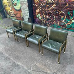 three green leather chairs sitting in front of a wall with graffiti on it's side