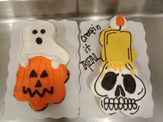 two decorated halloween cookies sitting on top of a metal counter covered in frosting and icing