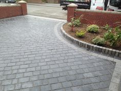 a brick paved driveway in front of a red brick wall and white van parked on the other side