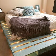 a bed made out of pallets with lights on the bottom and pillows on top