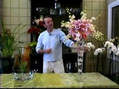 a man standing in front of a table with flowers on it and a vase filled with pink and white flowers