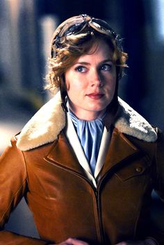 a woman in a brown leather jacket is looking at the camera