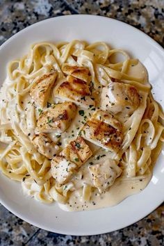 a white plate topped with pasta covered in sauce and chicken breast on top of it