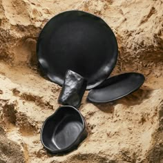 three black plates sitting on the ground next to each other in front of a rock