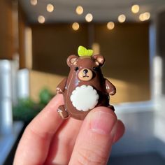 a hand holding a tiny brown bear with a green bow on it's head