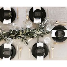 the table is set with black plates, silverware and greenery for an elegant touch