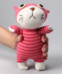 a hand holding a small pink and white cat doll with black eyes, wearing a red striped sweater