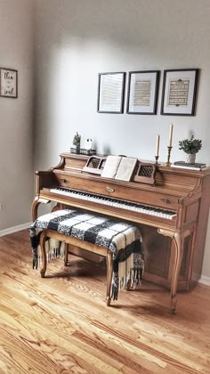 a piano sitting on top of a hard wood floor next to a wall with pictures above it