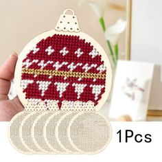 a hand holding a cross stitch ornament with four circles in front of it