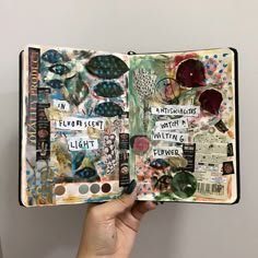 a hand holding an open book with many different things on it, including flowers and leaves