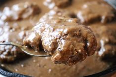 a spoon full of meat and gravy on top of a pan with sauce