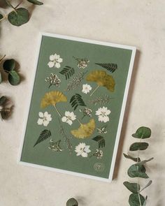 a card with leaves and flowers on it next to some eucalyptus branches in the background