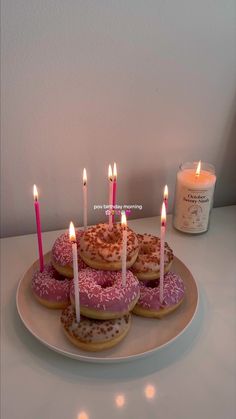 doughnuts with pink sprinkles and lit candles on a plate