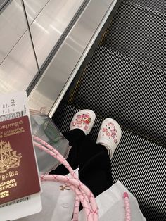 someone's feet in slippers next to a passport and some pink cords on an escalator