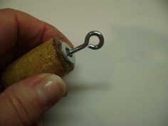 a person is holding a tiny cork with a metal hook on it's end