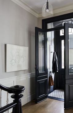 an entryway with black doors and wooden floors, white walls and artwork on the wall