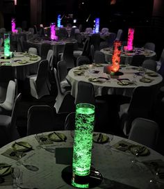 tables and chairs are lit up with colored lights in the dark, as well as vases filled with water