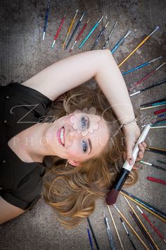 a young woman laying on the ground holding a brush and pencils in her hand