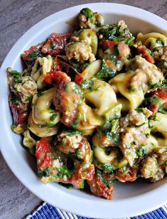 a white bowl filled with pasta covered in meat and vegtables on top of a table