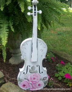 a white violin with pink flowers painted on it sitting in front of a planter