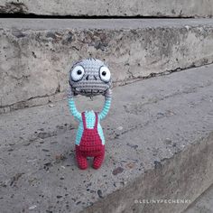 a crocheted stuffed animal is standing in front of some concrete steps with one eye open