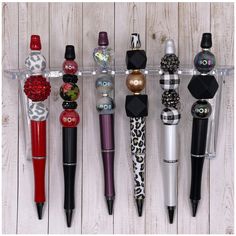 several different types of pens lined up in a row on a white wooden background with black and red accents