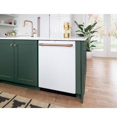 a kitchen with green cabinets and white counter tops, gold faucet pulls on the dishwasher