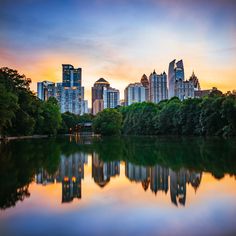 a city skyline is reflected in the water at sunset, with skyscrapers and trees on either side