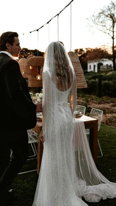 a bride and groom standing in front of a wooden table with lights strung from it