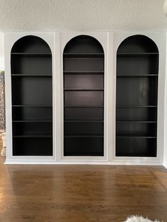 an empty room with three black bookshelves on the wall and wood flooring