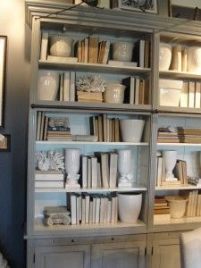 a book shelf filled with lots of books on top of a wooden floor next to a white chair