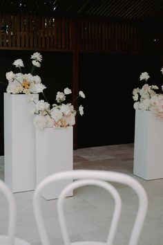 three white vases with flowers in them sitting on the ground